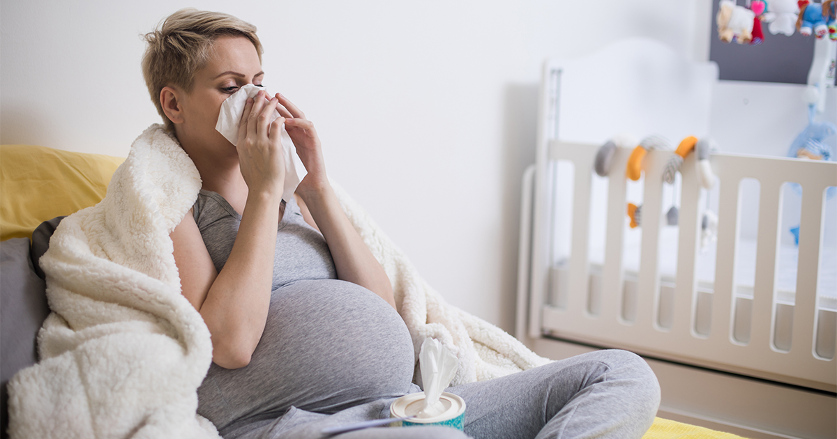 Pregnant woman blowing nose into tissue while sick at home