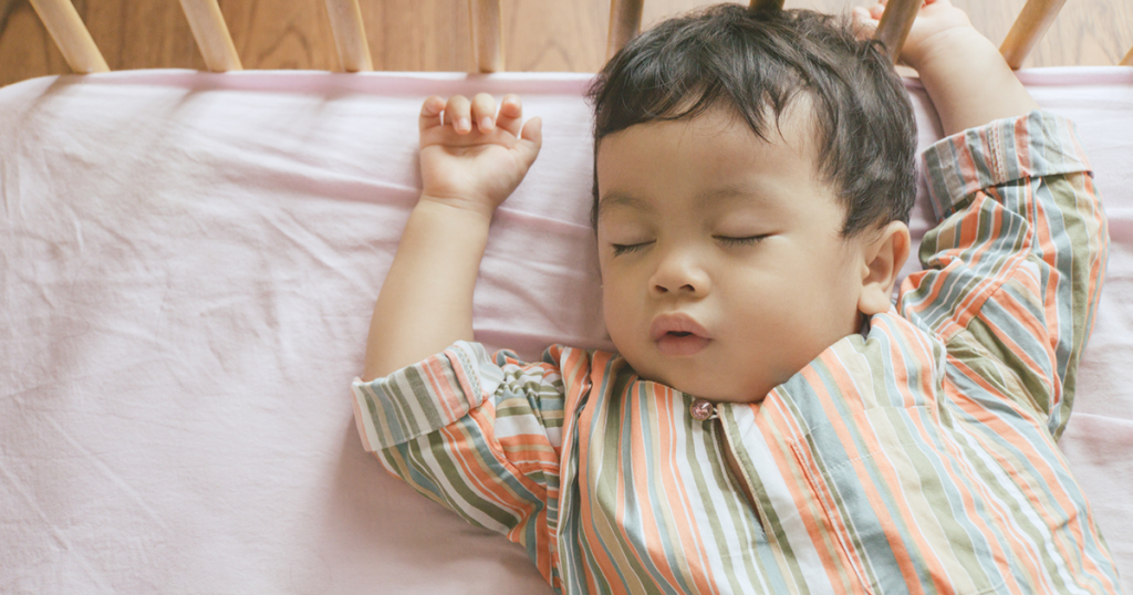 Little boy toddler adorably sleeping in his baby cot while wearing traditional Malay clothing, Ramadan and Eid concepts stock photo