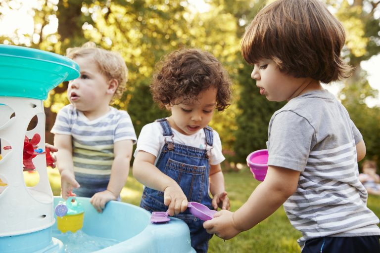 3 toddlers playing outside a water fountain toy.