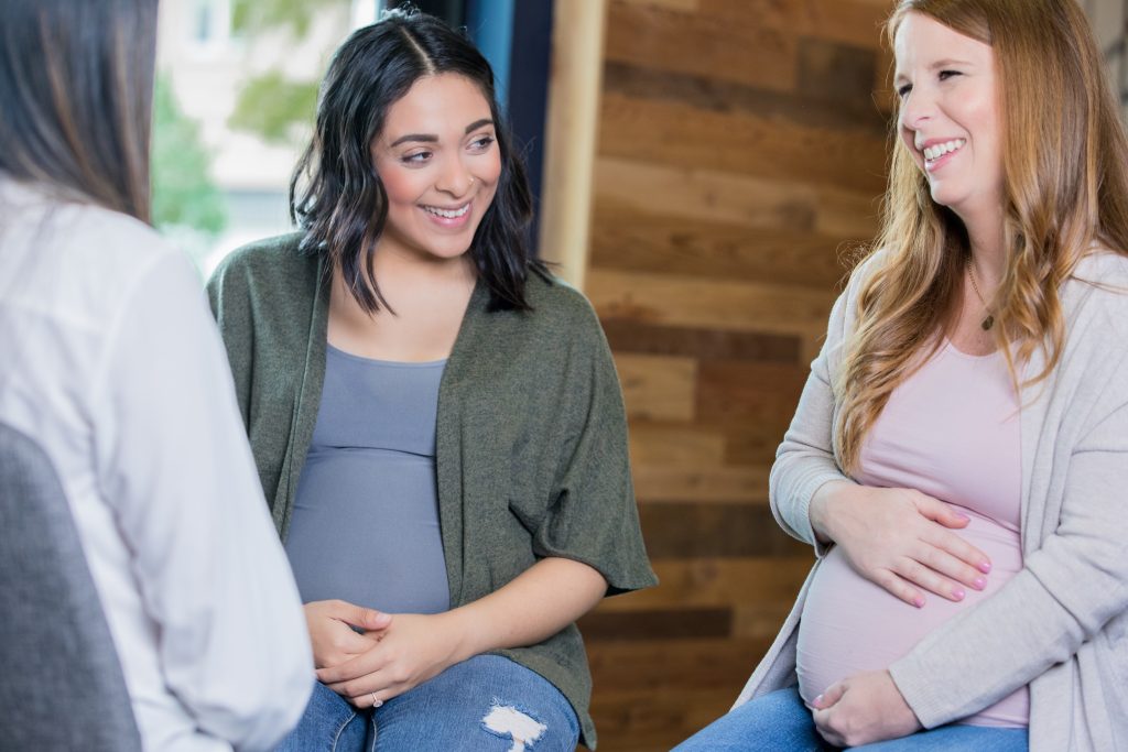 oung adult Hispanic and Caucasian expectant mothers are discussing their pregnancies during a childbirth class