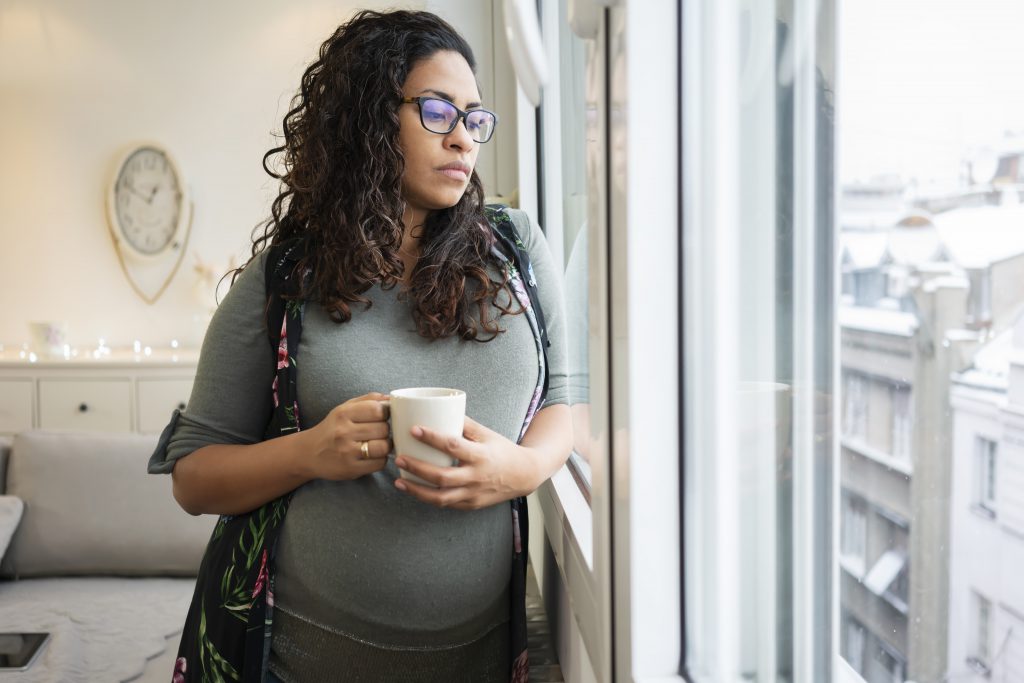 Sad pregnant woman drinking coffee at home