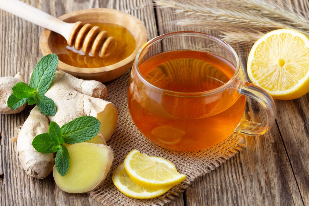 A glass cup of tea with lemon, mint, ginger and honey on wooden rustic table.