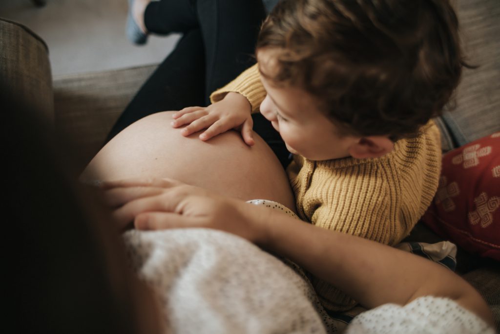 A little boy with light skin and dark hair touches his pregnant mother's belly.uches