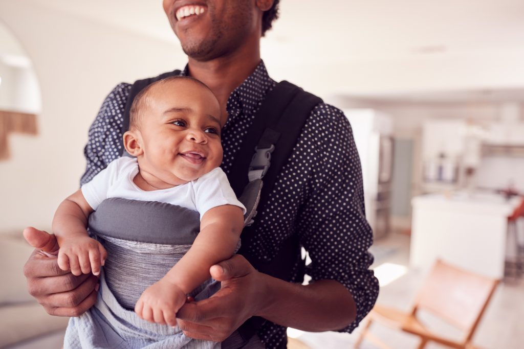 Close Up Of Father Playing With Smiling Baby Daughter In Sling At Home