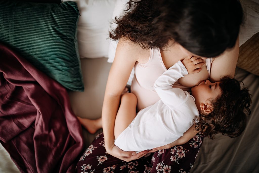 Mother breastfeeding her toddler child in cradle position.