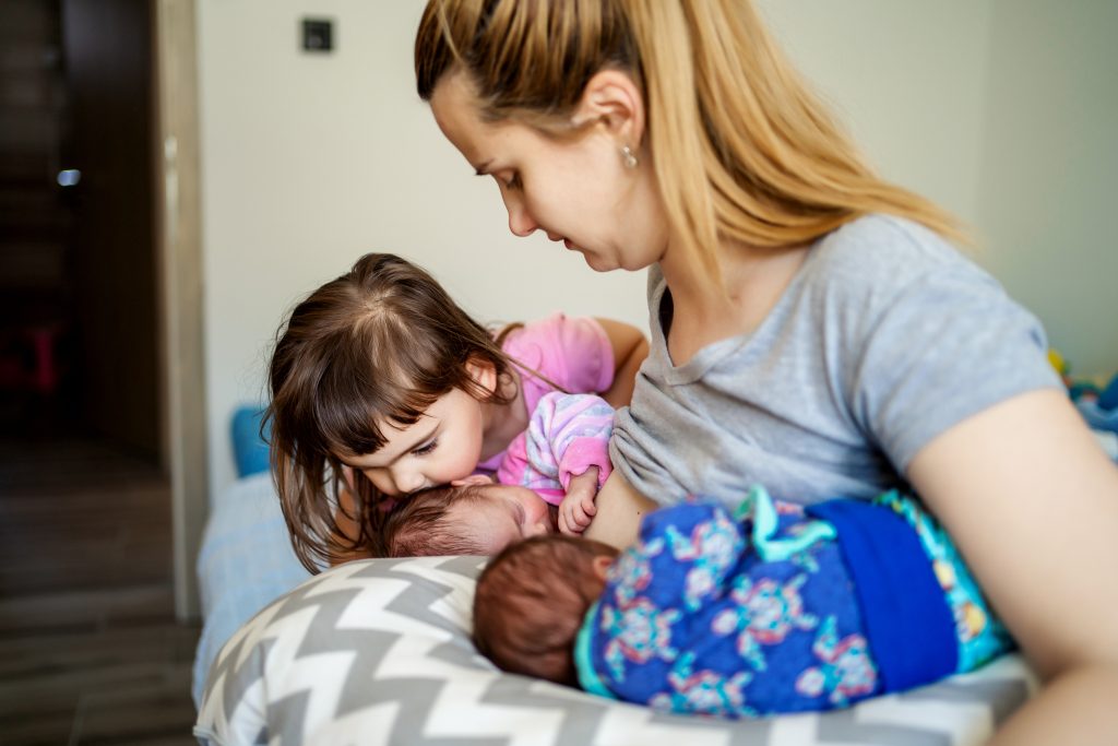 Mother is with her older daughter while breastfeeding her twin babies using double football hold.