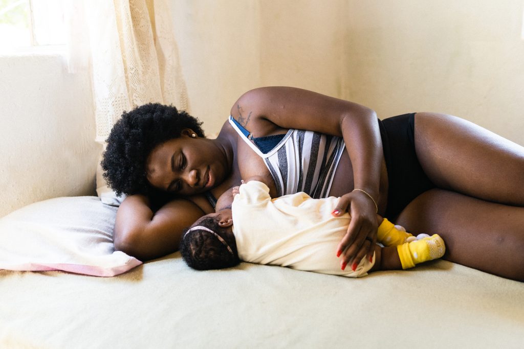 Mother in side-lying position breastfeeding in bed with newborn.