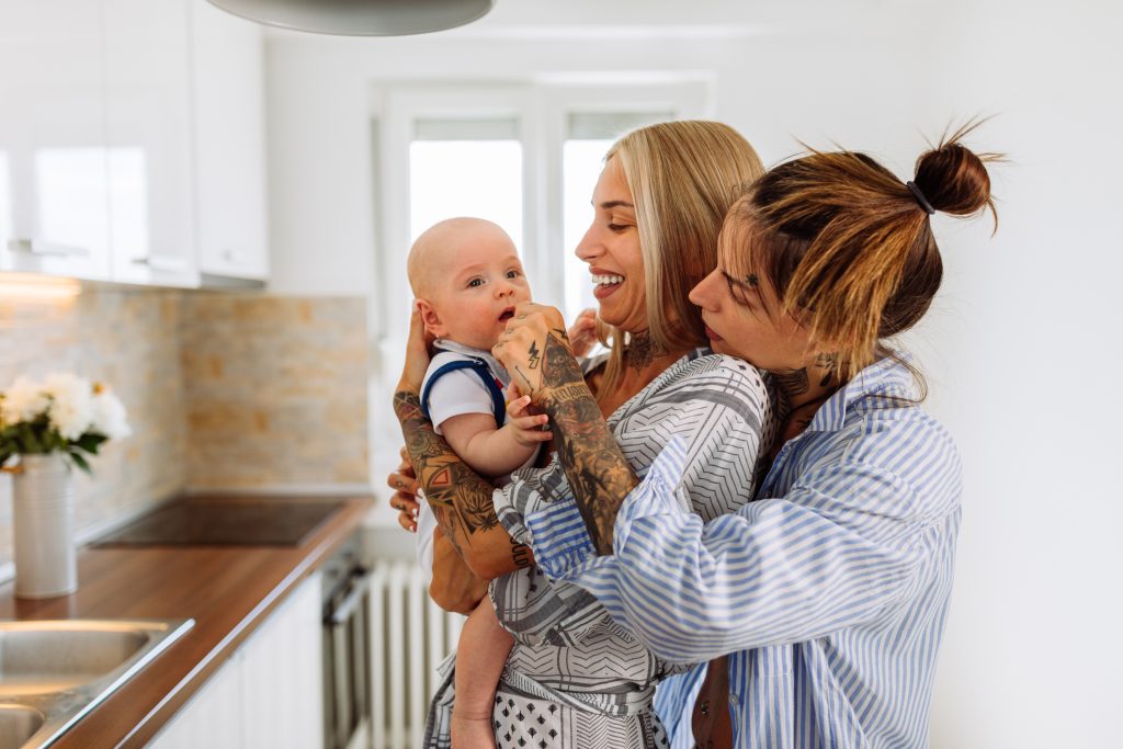 Loving lesbian couple playing with their baby while spending time together at home.