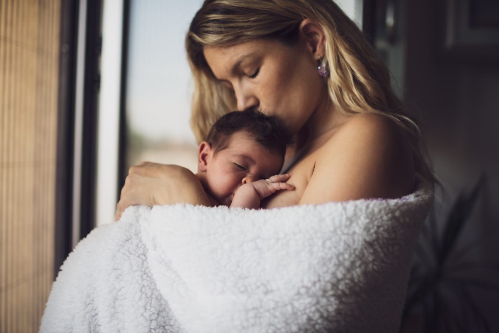 Young mother is holding her newborn baby girl wrapped in blanket while sleeping.