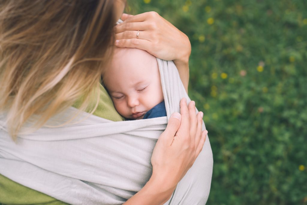 Woman carrying little child in baby sling in green mint color.