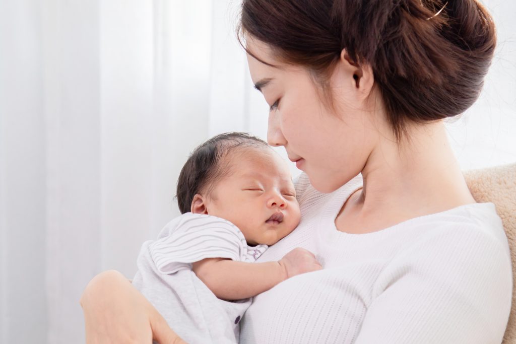 Closeup portrait of single mom asian looking newborn baby while sleeping. Mother holding her newborn in arm with love and care. adorable baby in arm her sleeping with happy and safe.