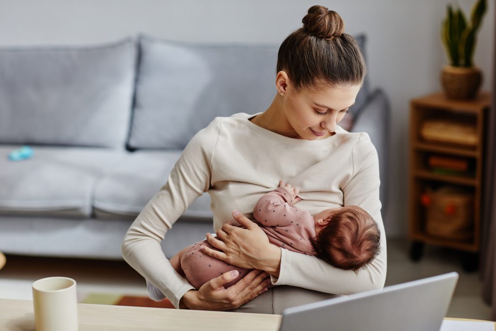 mother sitting by computer and lulling her baby during work break at home