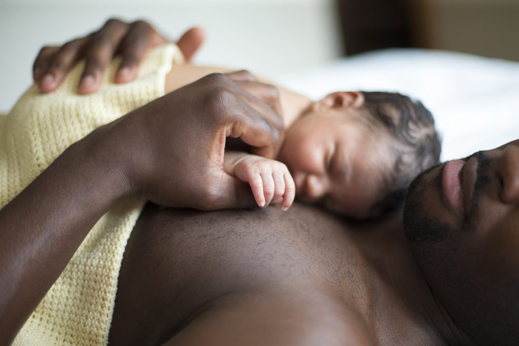 A father lying down with his newborn baby daughter sleeping on his chest.