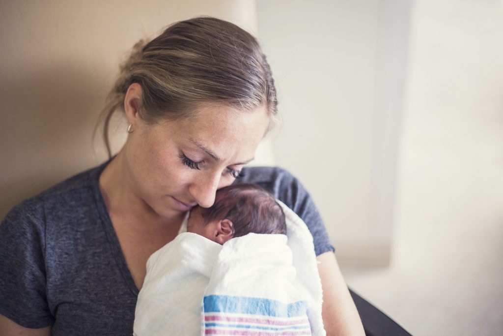 Young mother holding her Premature newborn baby who is being treated in the hospital. With love and tenderness she holds her baby close