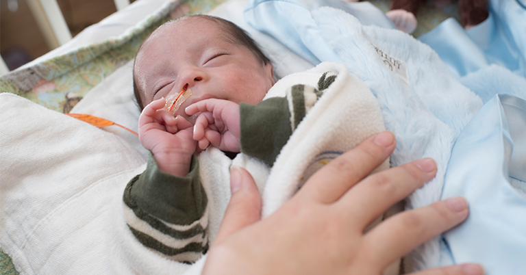 Image of a parent holding a newborn in the neonatal intensive care unit (NICU) of a hospital. 