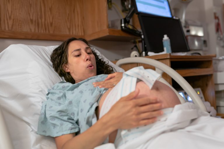 Mujer en una cama de hospital, con bata, haciendo ejercicios de respiración durante el trabajo de parto. Concentrada y tranquila.