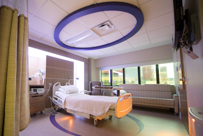 Photograph showing a typical patient room at the St. Paul location. Image shows a patient bed, a chair and a couch in the room.