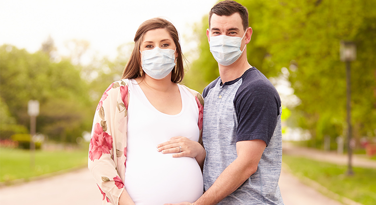Lauren Hall and her husband pregnant with masks on outside.