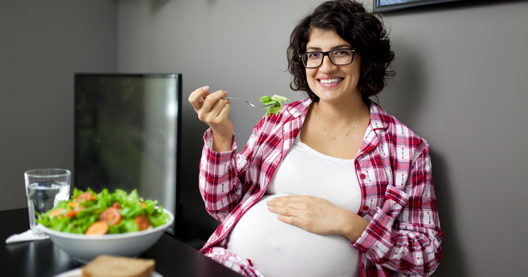 regnant woman at home eating a delicious healthy vegetable salad in her kitchen